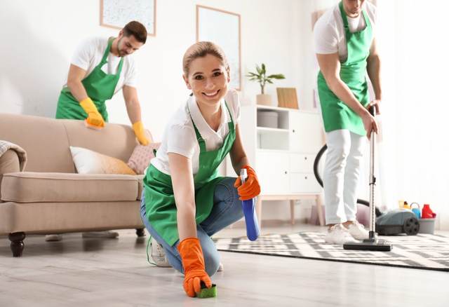 Cleaners in green aprons tidying and vacuuming a bright living room