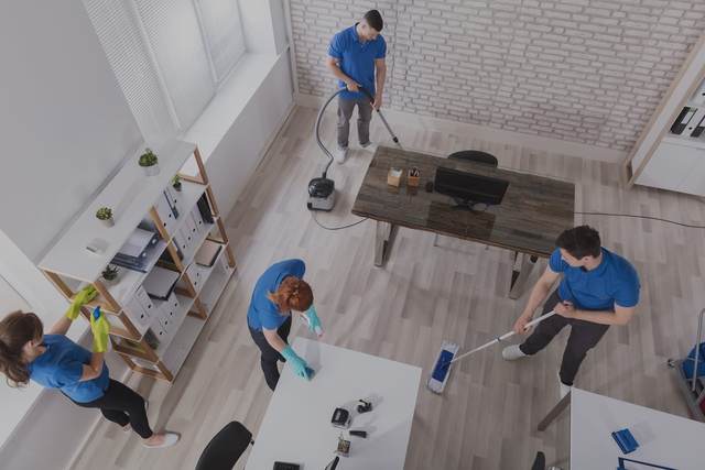 Cleaners vacuuming and wiping down an open-plan room, seen from above