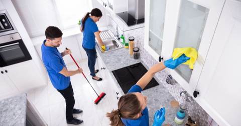 Three cleaners mopping, wiping and dusting in a kitchen, seen from above